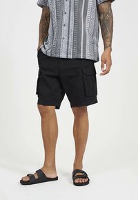 Svarta cargoshorts med flera fickor, gjorda av ett lätt material. Bärs med en mönstrad kortärmad skjorta och sandaler.