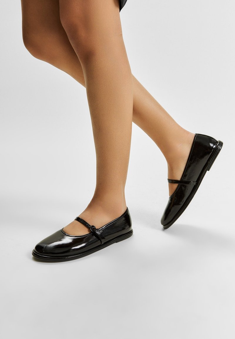 Zwarte gepatineerde leren balletschoenen met een afgeronde neus, voorzien van een decoratieve band en knoopdetail. Glad oppervlak en een laag profiel ontwerp.