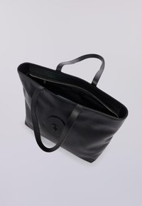 Černá kožená taška s dvěma dlouhými uchy, zipovým uzávěrem a kruhovým logem na přední straně. Hladký povrch a minimalistický design.