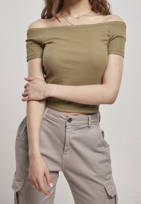 Top corto a coste color verde oliva con spalle scoperte abbinato a pantaloni cargo grigi chiari con tasche laterali e chiusura a bottone.