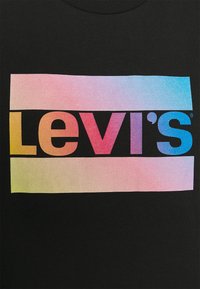 Musta puuvillapaita, jossa on pinkki, violetti ja sininen gradientti Levi's-logo, sijoitettuna suorakulmaiseen gradienttaustaan.