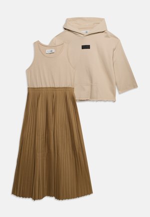Beige mouwloze top met bruine geplooide rok, gecombineerd met beige cropped hoodie met driekwart mouwen en voorzak.