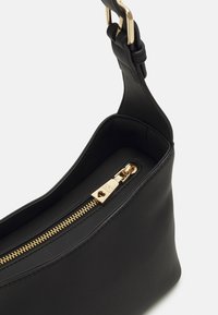 Sac à main en cuir noir avec une texture lisse, des fermetures éclair dorées et une forme structurée. Il dispose d'une bandoulière courbée et d'un intérieur spacieux.