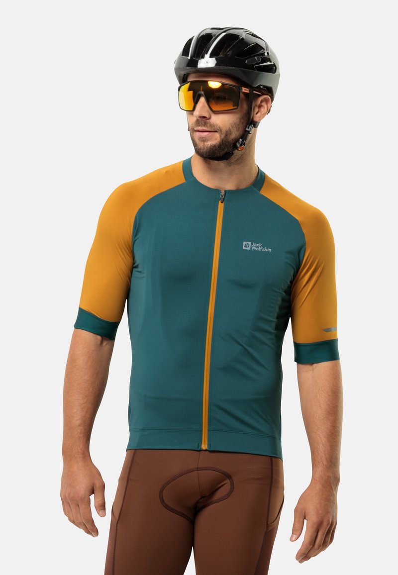 Fietsjersey in teal en oranje met korte mouwen, ritssluiting aan de voorkant en logodetail. Draagt met bruin gepolsterde shorts.