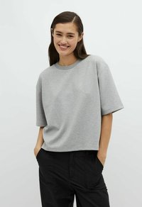 Grauer Kurzarm-Sweatshirt mit Rundhalsausschnitt und lässiger Passform, aus weichem Stoff gefertigt. Das Modell trägt dazu schwarze Hosen.