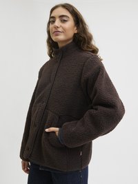 Pruun fliisjakkk, millel on kõrge krae, nööbiga kinnitamine ja eesmine taskud. Omab tekstuurset, pehmet pinda ja kontrastset viimistlust.