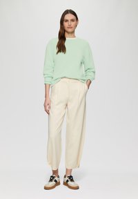 Mintgroene sweatshirt met opgerolde mouwen, gecombineerd met crèmekleurige plooibroek en zwart-witte sneakers, tegen een neutrale achtergrond.