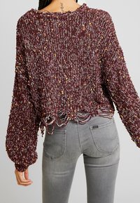 Burgunderfarbener Strickpullover mit mehrfarbigen Sprenkeln, cropped Design, lockere Passform und fransigem Saum. Lange Ärmel mit gerippten Bündchen.