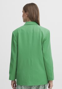 Blazer verde hecho de una tela suave. Presenta un diseño estructurado con solapas de muesca y mangas largas, mostrando un estilo limpio y minimalista.