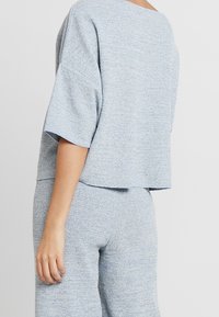 Haut en tricot bleu clair avec des manches larges, coupe décontractée, motif texturé, associé à un pantalon en tricot bleu clair assorti.