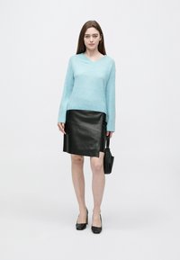 Svetlomodrý sveter s výstrihom do V vyrobený z mäkkej pleteniny kombinovaný s čiernou koženou sukňou po kolená s diagonálnymi švami. Čierne lodičky a kabelka.