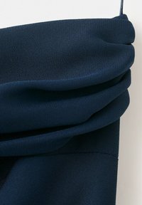 Temno mornarsko modra tkanina z mehkimi, plastnimi gubami in tankim trakom na vrhu, prikazana na belem ozadju.