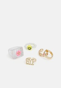 Quatro anéis: um anel de resina transparente com uma flor rosa, uma contas com um rosto sorridente amarelo, um anel dourado com "BYE" e uma aliança dourada decorativa com acentos.