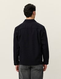 Μπλε ναυτικού πουκάμισο, μακριά μανίκια, κολάρο, κουμπωτές μανσέτες, απλό ύφασμα, η πίσω όψη δείχνει τις ραφές στους ώμους και ελαφριά καμπύλη στο στρίφωμα.