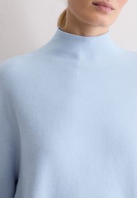 Maglione a maglia blu chiaro con collo alto, caratterizzato da una lavorazione a coste e una silhouette rilassata. Nessun motivo visibile o dettagli in metallo.
