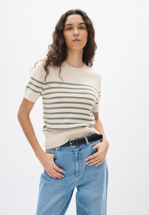 Beige striped knit sweater with short sleeves and rounded neckline. Features horizontal olive green stripes. Worn with light blue jeans and black belt.