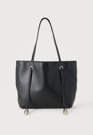 Sac fourre-tout en cuir noir avec deux fines bretelles et des cordons décoratifs avec embouts métalliques argentés sur fond blanc.