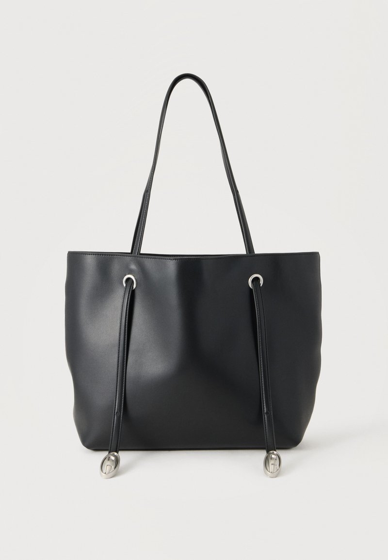 Sac fourre-tout en cuir noir avec deux fines bretelles et des cordons décoratifs avec embouts métalliques argentés sur fond blanc.