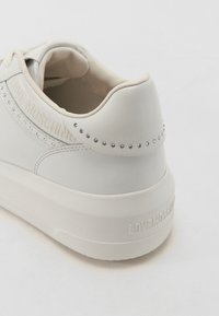 Valge nahast tennisekenad, millel on nurgelised detailid, pehme krae ja paks tall. "LOVE MOSCHINO" on alla ja küljele pressitud. Sile tekstuur.