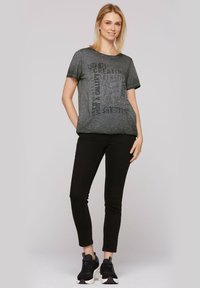 Szara koszulka graficzna z czarnymi wzorami tekstowymi, krótki rękaw, okrągły dekolt, w połączeniu z czarnymi spodniami slim fit i czarnymi sneakersami.