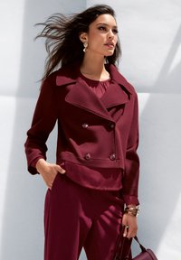 Bordeaux, dubbelgeknoopte blazer met brede revers, textuurstof en twee knopen aan de voorkant. Gecombineerd met een bijpassende top en broek.