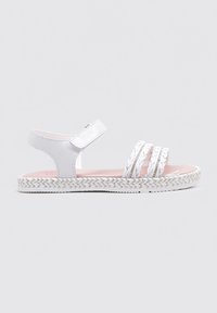 Sandal blanco con tres correas trenzadas, correa ajustable en el tobillo y una suela texturizada y tejida. Plantilla rosa visible.