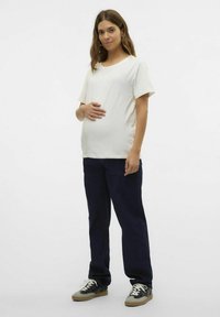 Cremefarvet graviditets T-shirt med korte ærmer, afslappet pasform, parret med mørkeblå brede bukser og sort-hvide sneakers på en lys baggrund.