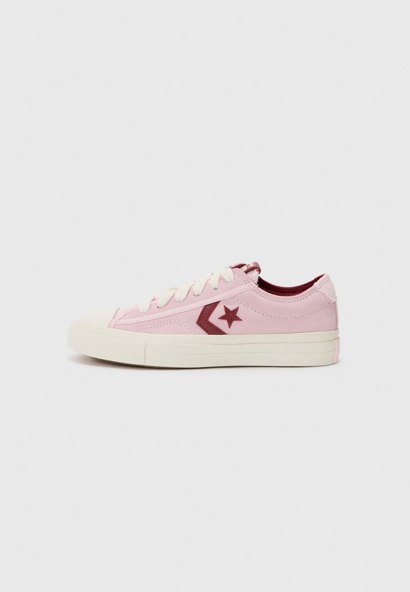 Light pink sneakers with a textured canvas upper, cream laces, and red accents, including a star logo and a rubber toe cap.
