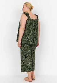 Completo a due pezzi con stampa leopardata verde, dotato di spalline arricciate e pantaloni a gamba larga. Il materiale sembra leggero, con una vestibilità comoda e un scollo elasticizzato.