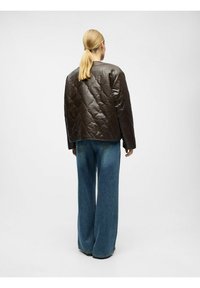 Braune gesteppte Lederjacke mit kastiger Form, abgerundeten Schultern und einem gerippten Ausschnitt. Kombiniert mit weitem blauen Denim-Jeans.