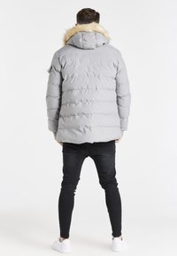 Graue Daunenjacke mit einer Kunstpelzkapuze, ausgestattet mit horizontaler Steppstruktur. Trägt man über schwarzen engen Jeans und weißen Sneakers.