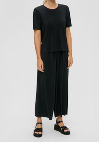 Top negro de punto acanalado con mangas cortas, combinado con pantalones sueltos negros a juego. Lleva sandalias de plataforma negras con detalle de hebilla.