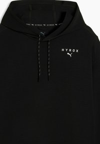 Μαύρο φούτερ με κουκούλα, με τυπωμένα μπροστά τα λογότυπα "HYROX" και Puma, διαθέτει κορδόνια και εσωτερική ταινία με επωνυμία στη γραμμή του λαιμού.