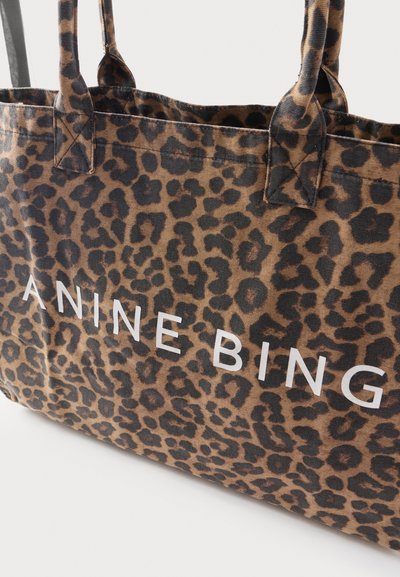 Bolso tote con estampado de leopardo con manchas negras y marrones, con texto blanco "ANINE BING" y asas de tela resistentes.