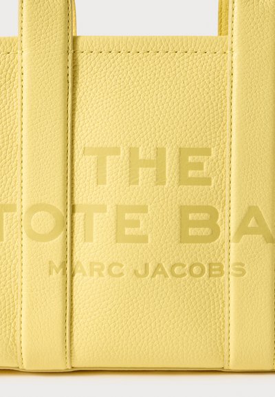 Gelbe Leder-Tasche mit strukturierter Oberfläche. Mit großem geprägtem Text: "THE TOTE BAG" und "MARC JACOBS." Robuste obere Tragegriffe.