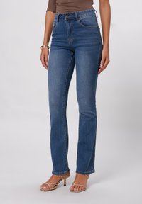 Hochtaillierte blaue Jeans, die an den Hüften eng anliegen und sich am Knöchel leicht ausstellen, mit Fronttaschen und Knopfverschluss. Glattes Denimgewebe.