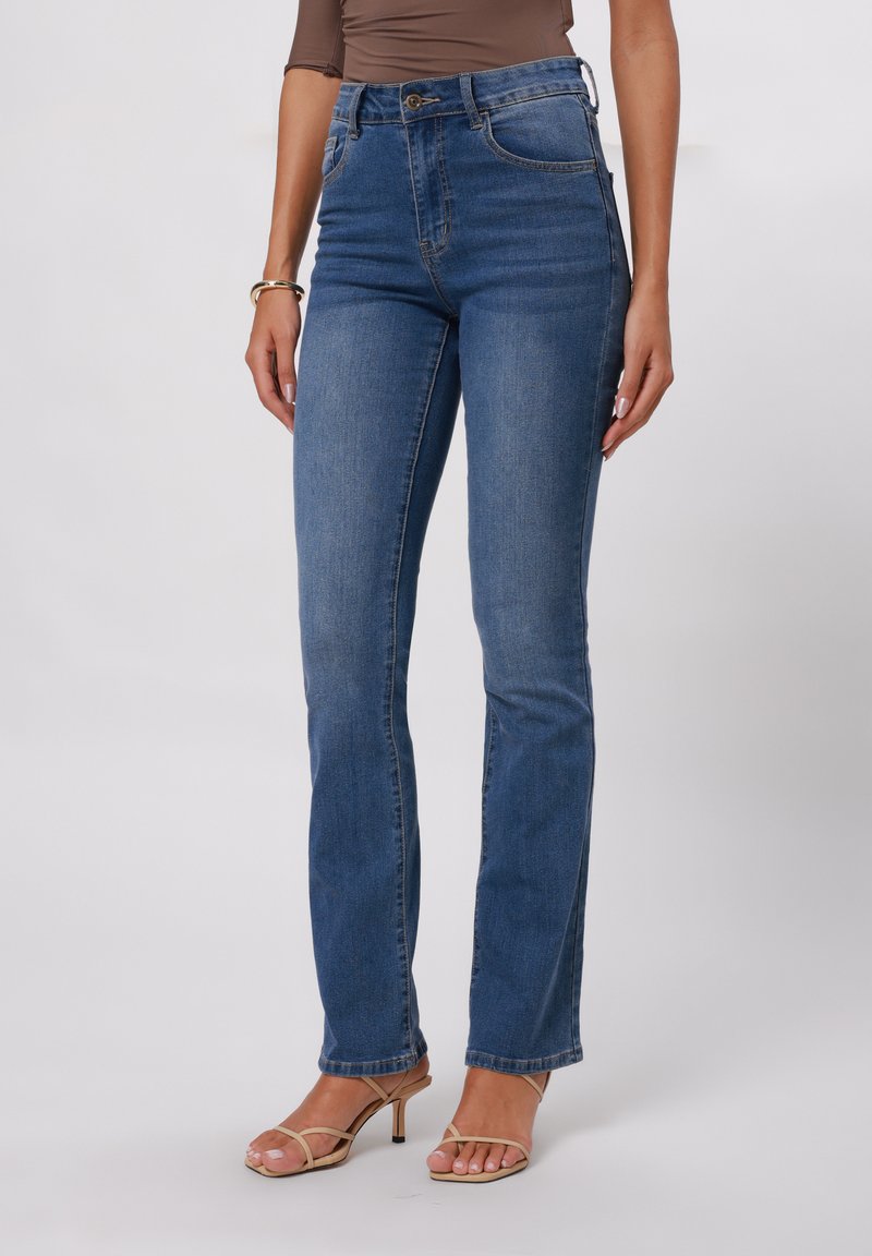 Hochtaillierte blaue Jeans, die an den Hüften eng anliegen und sich am Knöchel leicht ausstellen, mit Fronttaschen und Knopfverschluss. Glattes Denimgewebe.