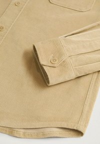 Beige fløjlsskjorteærme med knaplukning og matchende knapper synlige foran, der viser ribbet stofstruktur og buet kant.