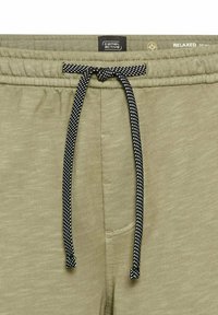 Olivengrønne sweatpants med en sort-hvid prikket snor. Har en elastisk talje og en afslappet pasform med en glat struktur.