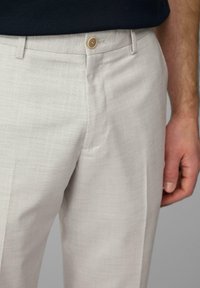 Helle beigefarbene Hosen aus strukturiertem Stoff, taillierte Passform und ein Einzelknopfverschluss; mit Seitentaschen und einem dezenten gewebten Muster.