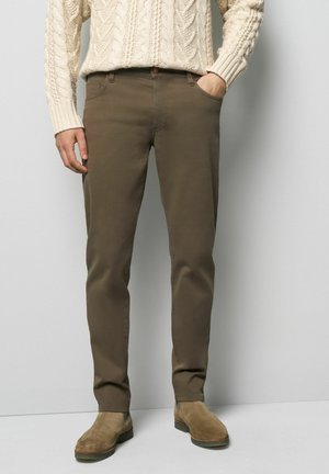 Pantalons en coton marron à coupe droite, avec poches avant et fermeture par bouton, accompagnés de bottines en daim beige à la cheville.