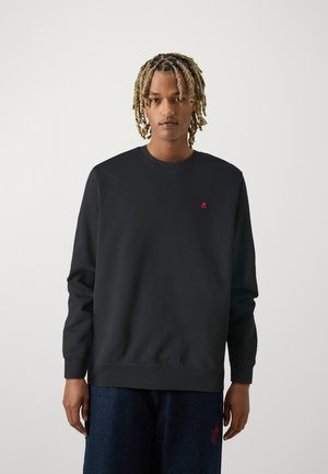 Sudadera negra con cuello redondo y mangas largas. Presenta un pequeño logo rojo en el pecho. El material parece suave y tiene un ajuste relajado.