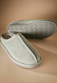 Chaussons en suède gris avec une doublure intérieure douce, présentant un bout arrondi, des détails cousus et une semelle texturée pour une meilleure adhérence.