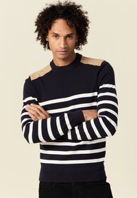 Maglione a righe navy con strisce orizzontali bianche e accenti beige sulle spalle. Presenta un collo a giro e polsini a coste per un look aderente.