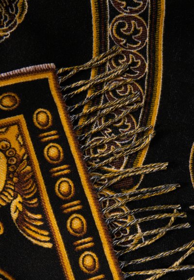 Υφαντό ύφασμα σε μαύρο και χρυσό με περίπλοκα σχέδια, κυκλικά μοτίβα και στριφτές άκρες με κρόσσια.