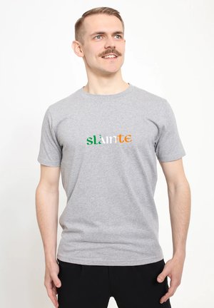 Šedé bavlněné tričko s nápisem "slàinte" v zelené, bílé a oranžové barvě umístěným napříč hrudníkem, s kulatým výstřihem a krátkými rukávy.