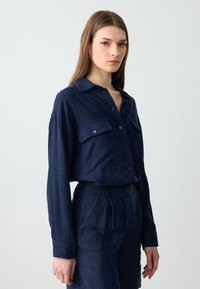 Marineblaue Hemdbluse mit zwei Brusttaschen, langen Ärmeln und klassischem Kragen. Hergestellt aus einem strukturierten Stoff, der eine lockere Passform bietet.