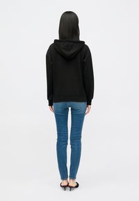 Sweatshirt preto com capuz, de corte solto, tecido texturizado e punhos canelados. Combinado com jeans skinny azuis e saltos pretos.