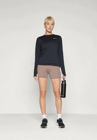 Nike majica dugih rukava, tamnoplava boja, u kombinaciji s smešnim šortsevima. Crni patike, bijele čarape, drži crnu bocu vode. Jednostavan sportski dizajn.