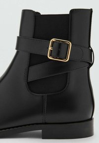 Botine negre cu un finisaj din piele netedă, panou lateral elastic și o curea decorativă cu cataramă aurie. Talpă plată și design cu vârf rotund.